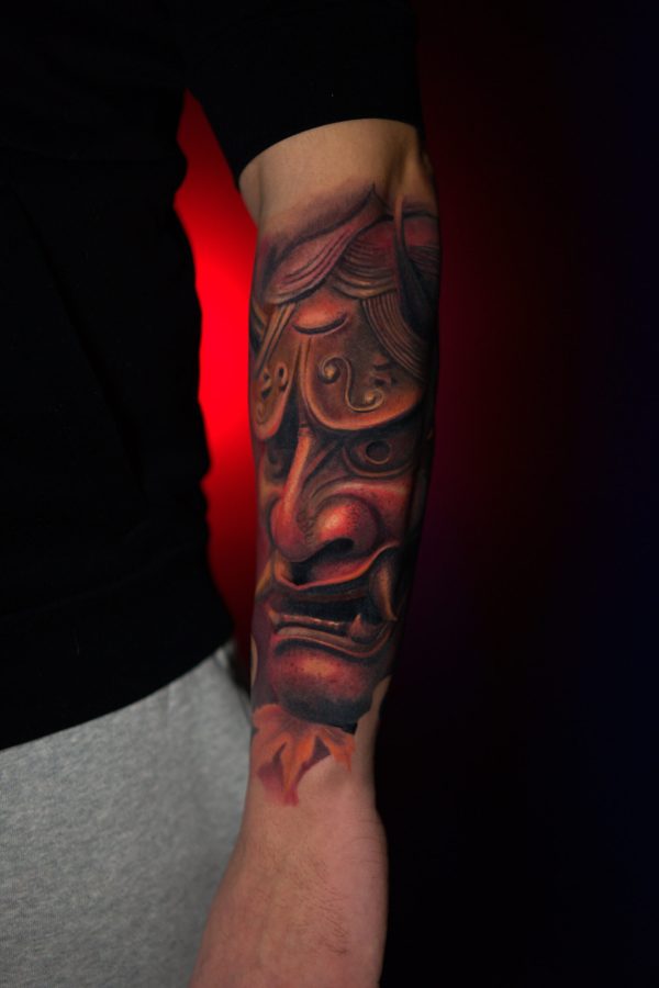 realistic hannya mask color tattoo with red tones on forearm by Mihaly Forgony